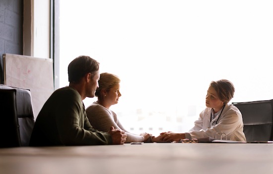 A photo of female doctor comforting couple. Mid adult partners consulting from medical professional. They are at doctor's office.