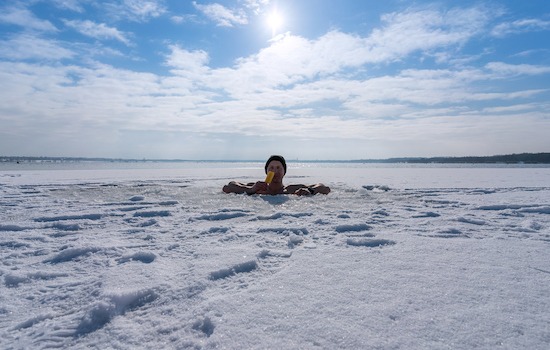 Man sitting in an ice hole while eating ice cream in winter
