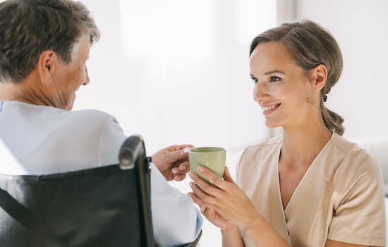 Young caring nurse helping older woman with a tea