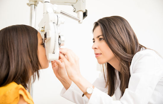 Pretty optometrist adjusting phoropter for child patient in store