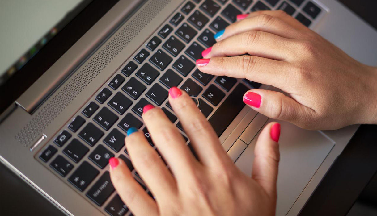 Zwei Hände mit bunt lackierten Fingernägeln tippen auf einer Tastatur