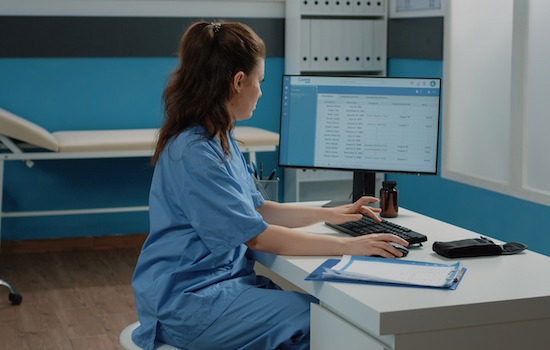 Woman working as nurse with computer and documents in cabinet, checking files for examination appointment. Medical assistant looking at screen for patient information and checkup visit