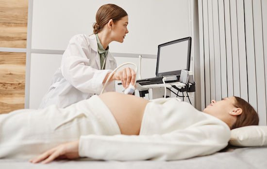 Portrait of female doctor performing ultrasound exam on pregnant young woman in modern medical clinic