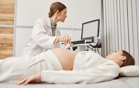 Portrait of female doctor performing ultrasound exam on pregnant young woman in modern medical clinic