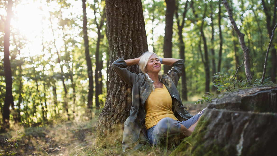 A portrait of senior woman relaxing and sitting with eyes closed outdoors in forest.