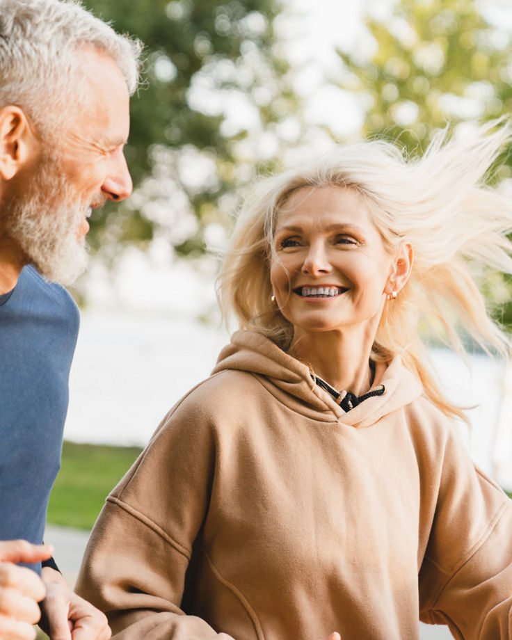 Mature middle aged senior couple running together in the park stadium looking at each other while jogging slimming exercises. Training workout