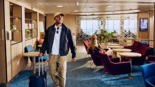 Uśmiechnięta pasażerka z walizką wchodzi do salonu Stena Plus na pokładzie, ciesząc się spokojną podróżą promem.