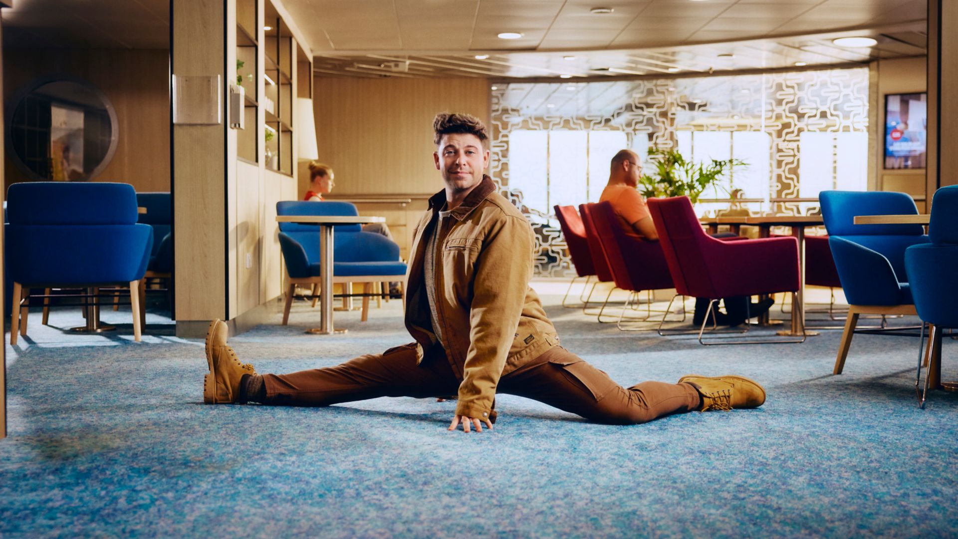 Man die de spagaat doet in een stijlvolle lounge aan boord van een Stena Line ferry, omringd door ontspannen passagiers