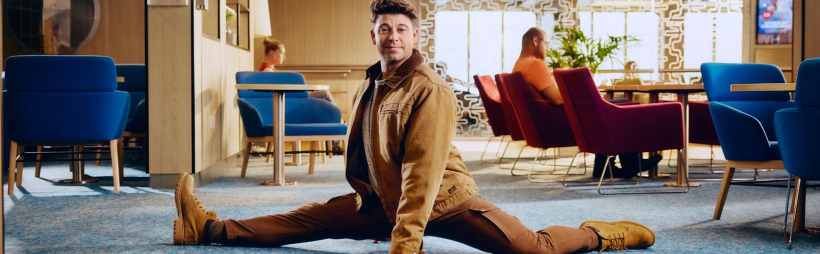 Man die de spagaat doet in een stijlvolle lounge aan boord van een Stena Line ferry, omringd door ontspannen passagiers