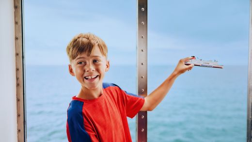 Dziecko uśmiecha się w salonie na promie, trzyma zabawkowy statek Stena Line i cieszy się podróżą