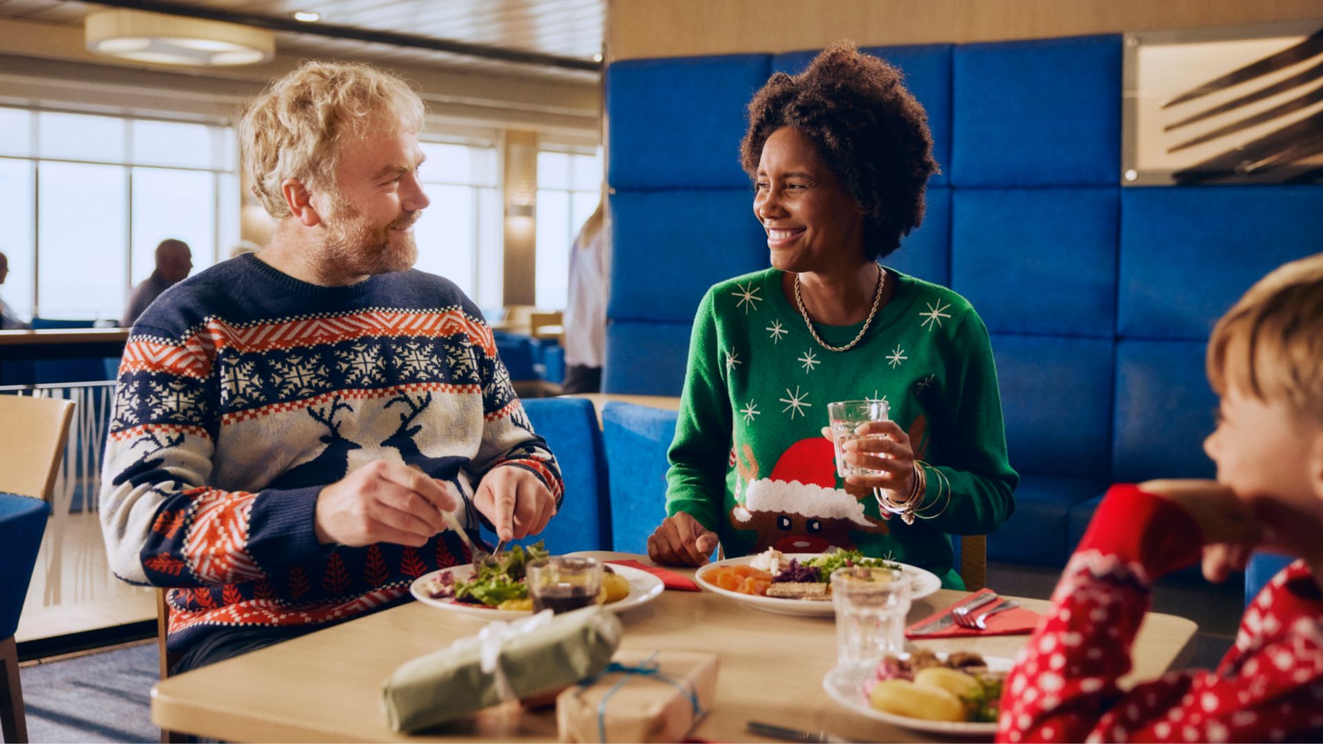 Family enjoying Christmas buffet onboard ferry in festive jumpers during their holiday crossing