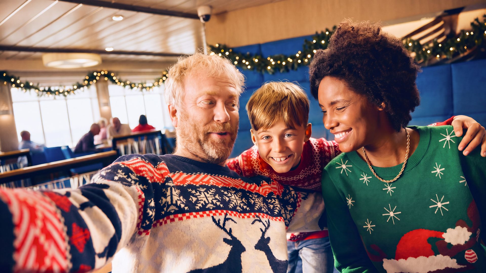 AI-genererad bild. En leende familj på tre personer poserar tätt ihop för en selfie, iklädda färgglada jultröjor. De befinner sig inomhus med girlanger och blinkande ljusslingor i bakgrunden, vilket skapar en julig stämning. Pappan håller i kameran på uts