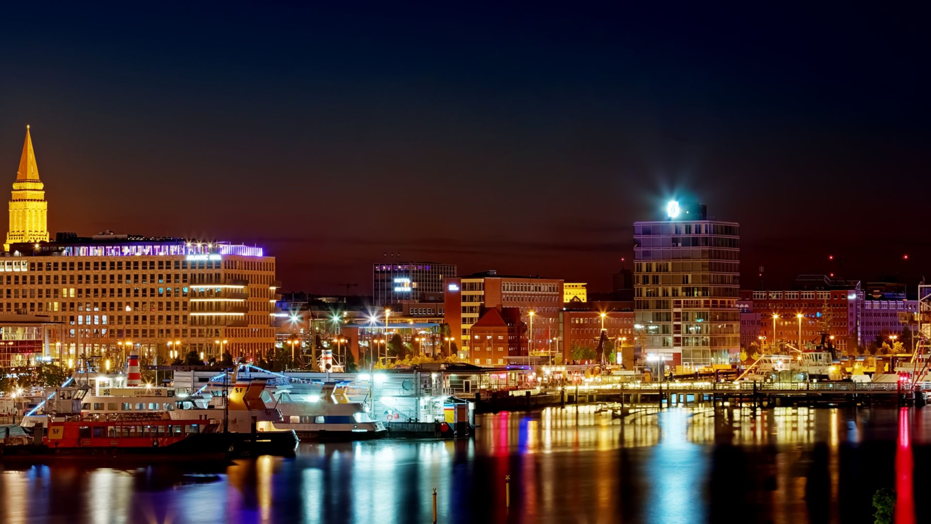 The waterscape of Kiel Harbour at night  with the lights of the ships and buildings reflected in the calm waters.