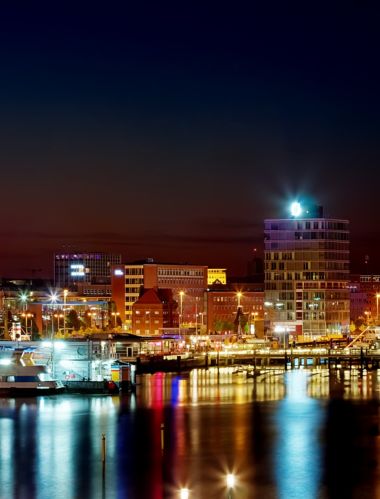 The waterscape of Kiel Harbour at night  with the lights of the ships and buildings reflected in the calm waters.