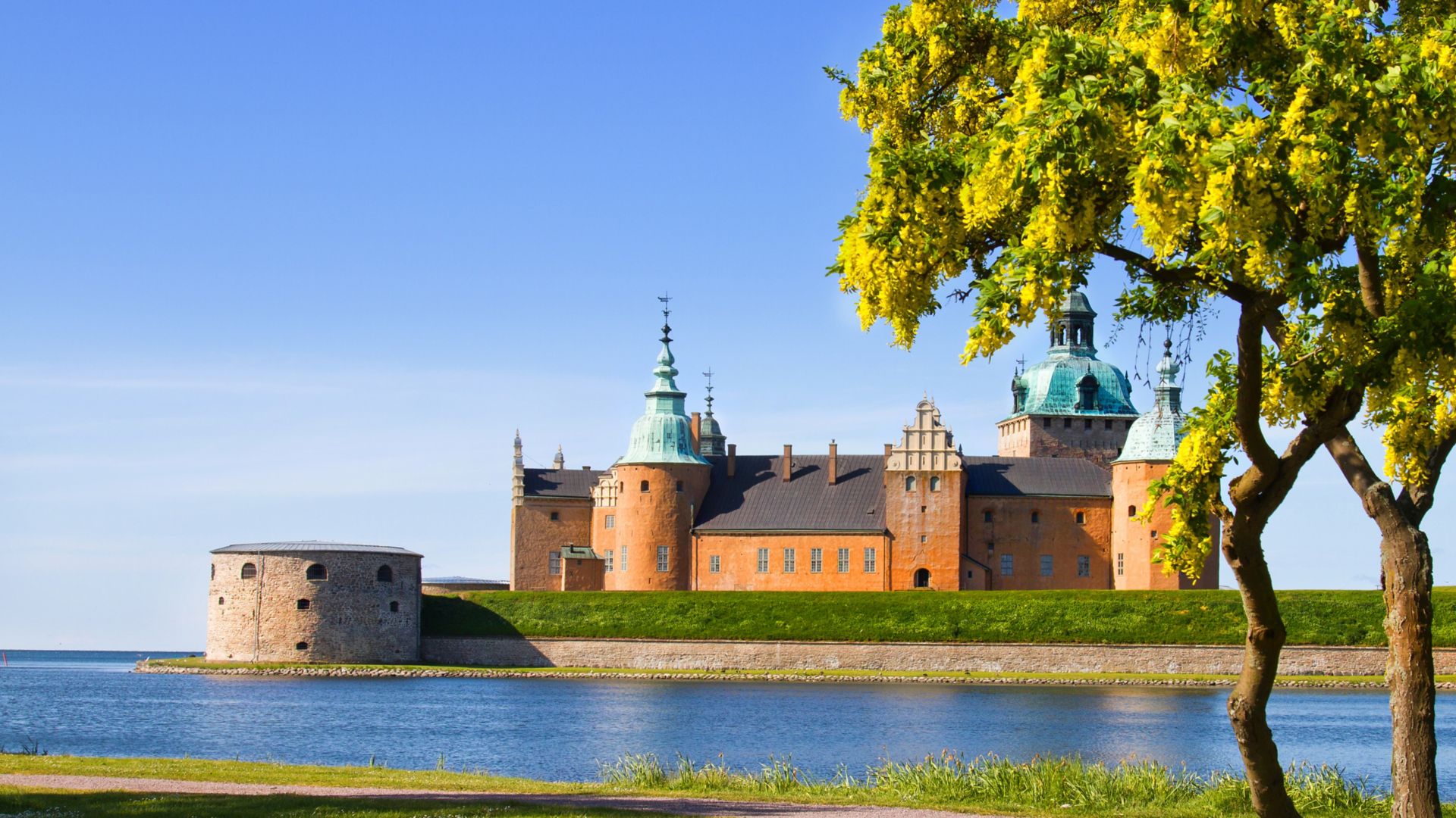 Viduramžių pilis su raudonomis sienomis ir mėlynais bokšteliais, apsupta vandens giedrą saulėtą dieną Kalmare, Švedijoje.