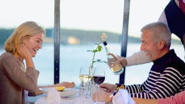 Uśmiechnięta para, której kelner podaje wino w restauracji à la carte na pokładzie promu