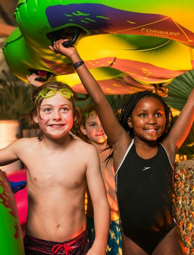 Børn, der bærer vandflåder over en rebbro ved den indendørs pool på Reef Resort