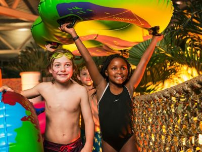 Børn, der bærer vandflåder over en rebbro ved den indendørs pool på Reef Resort