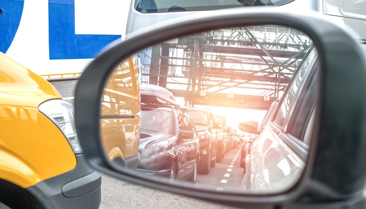 Blick über den Außenspiegel eines Autos auf Fahrzeuge, die auf einer Autospur auf das Boarding einer Stena Line Fähre warten