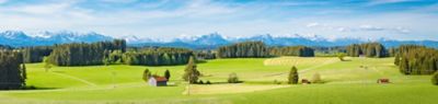 Allgäu, red roofed farm buildings on a vast green landscape  of fields and forest with a dramatic backdrop of snow capped mountains on the horizon