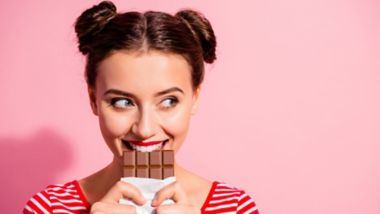 Kvinde smiler, mens hun tager en bid af en chokoladebar