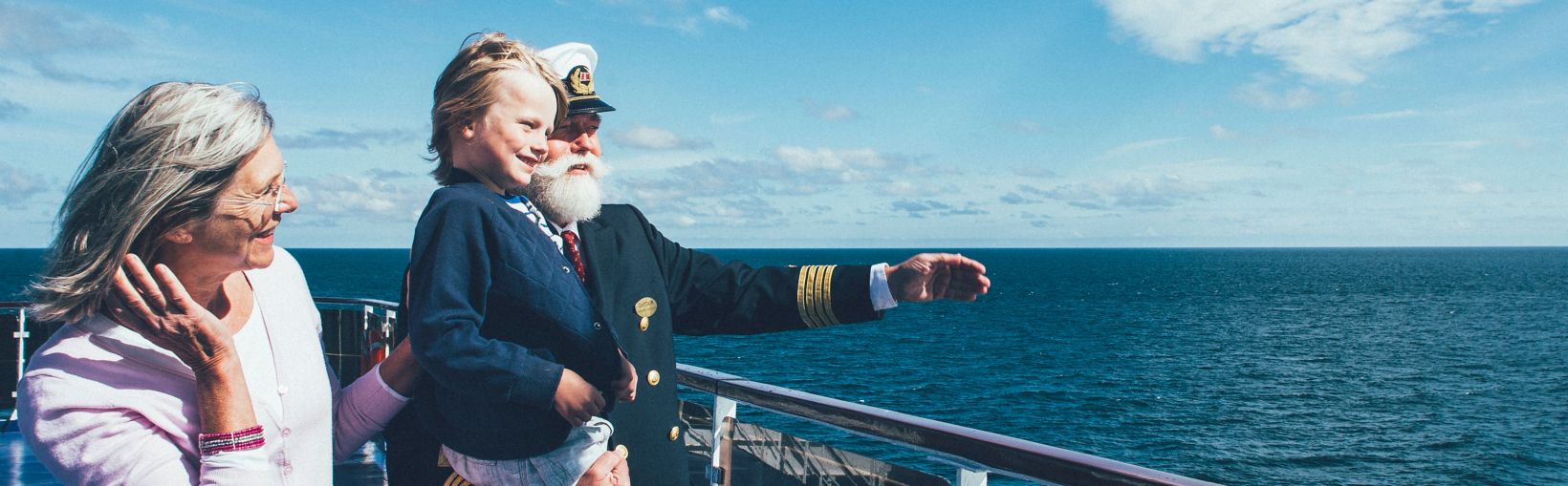 The captain of a Stena Line ferry on deck pointing out to sea and holding a young boy with his mother smiling nearby