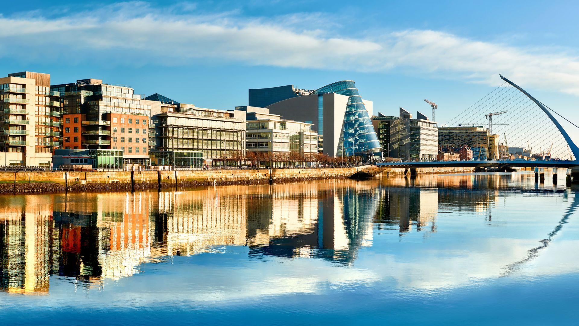 Kaasaegsed hooned ja kontorid Liffey jõel Dublinis eredal päikesepaistelisel päeval, Harpi sillaga paremal