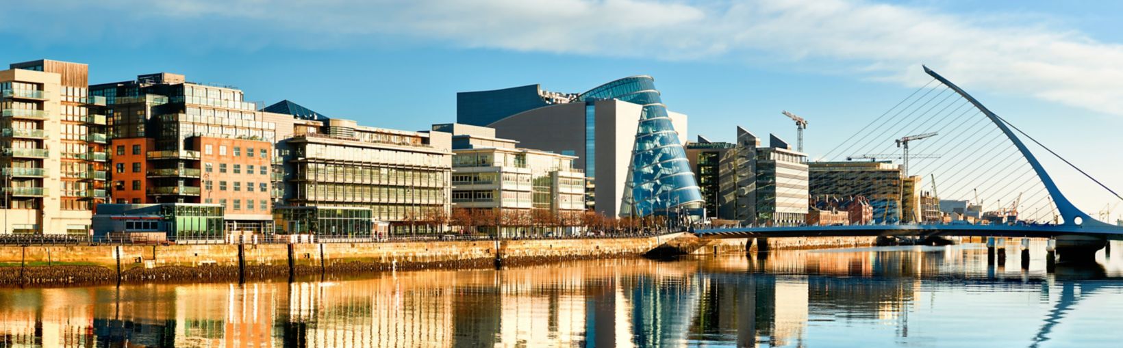 Moderne bygninger og kontorer på Liffey-floden i Dublin på en solrig dag med Harp-broen til højre