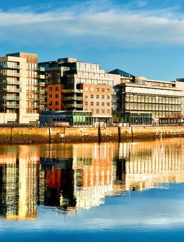 Modern buildings and offices on Liffey river in Dublin on a bright sunny day, with Harp bridge on the right