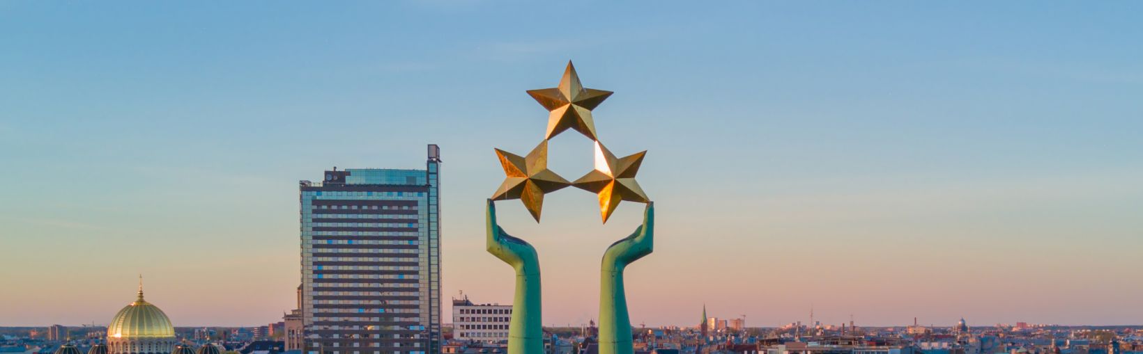 Przepiękny widok zachodu słońca w Rydze obserwowany przy Pomniku Wolności Milda. Wolność na Łotwie. Pomnik Wolności z kobiecą postacią unoszącą nad miastem trzy gwiazdy