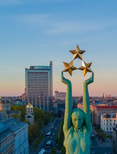 Przepiękny widok zachodu słońca w Rydze obserwowany przy Pomniku Wolności Milda. Wolność na Łotwie. Pomnik Wolności z kobiecą postacią unoszącą nad miastem trzy gwiazdy