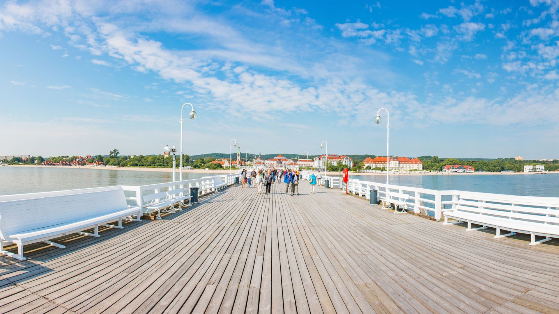 En vidvinkelvy över träpiren som blickar tillbaka mot byggnaderna med orange tak vid stranden.