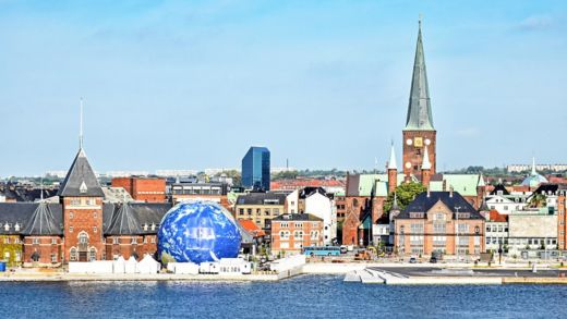 Aarhaus stadssilhuett från hamnområdet med byggnader, kupoler, kranar och höghus.