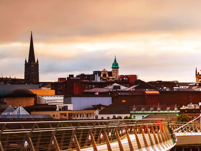 Derry, Ireland. Illuminated Peace bridge in Derry Londonderry in Northern Ireland with city center at the background. Night cloudy sky, reflection in the river.