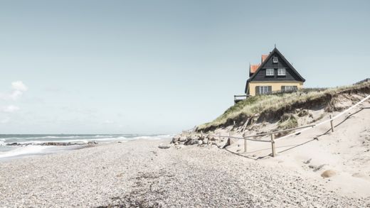 Lugn strandmiljö med orörda blått vatten, sandstrand och strandhus under en solig himmel.