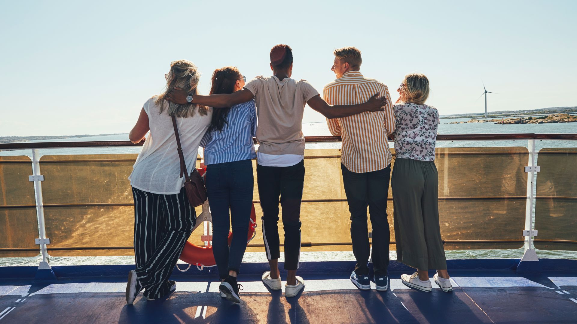 View from behind of a group of 5 friends on the sundeck of a ferry looking out to sea