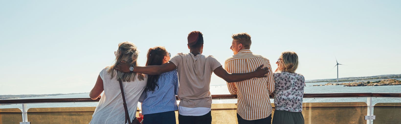 Vy bakifrån av fem vänner som tittar ut mot havet från soldäcket på en färja