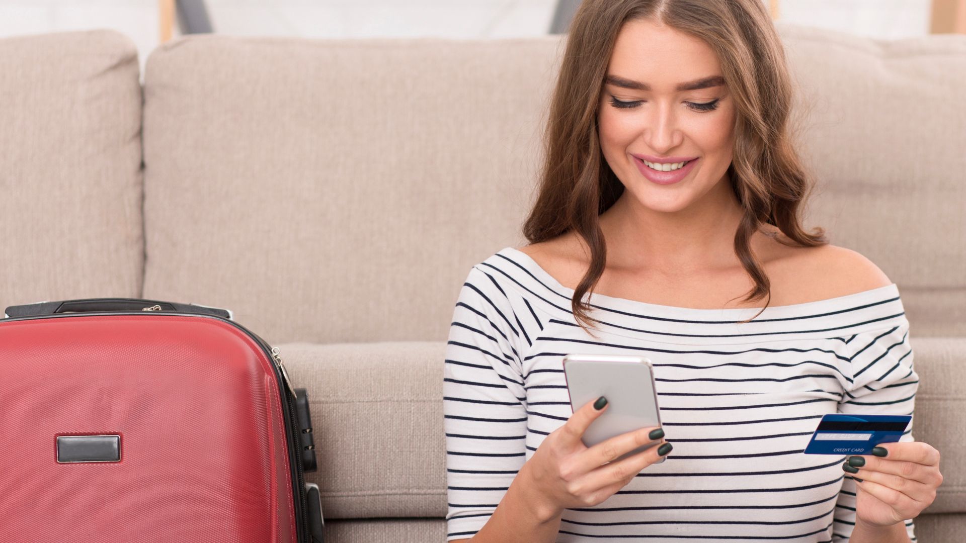 Buying tour online. Girl preparing for vacation, using phone and credit card at home