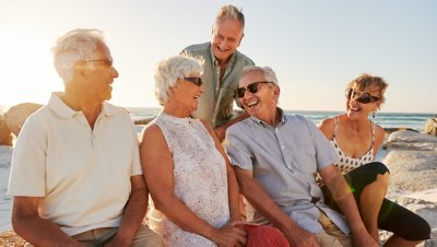 En gruppe ældre venner, som er på sommerferie og sidder på nogle sten ved havet