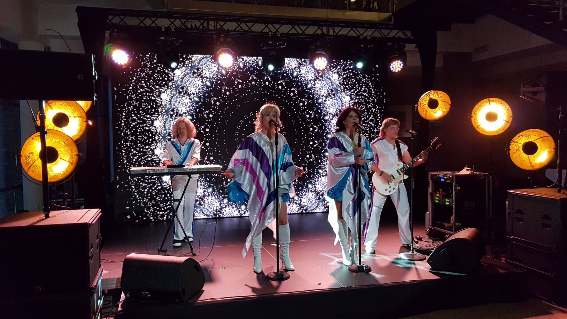 Trzech mężczyzn śpiewających z entuzjazmem karaoke z piosenkami ABBA podczas rejsu Stena Line, w radosnej atmosferze imprezy na pokładzie.