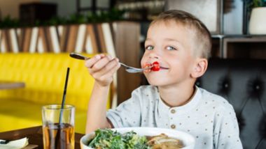 Zadowolony chłopiec jedzący posiłek w restauracji