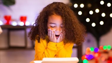 Desired present. Amazed little afro girl opening Christmas gift near xmas tree, free space