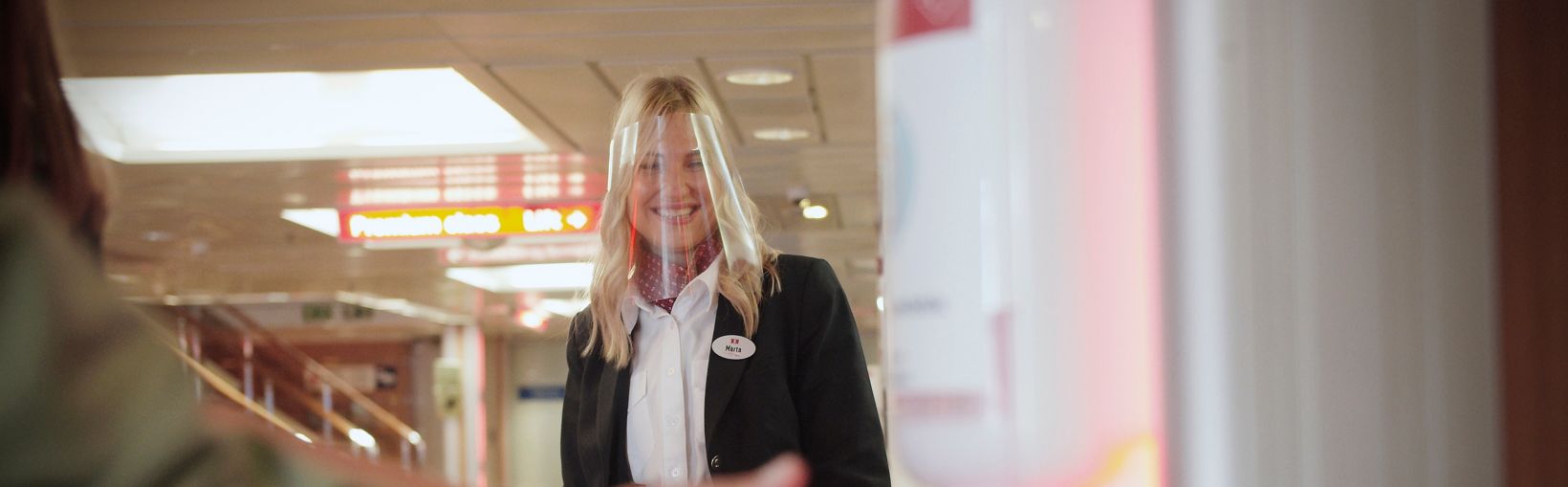 Smilende Stena Line-medarbejder, der ser en passager bruge dispenseren til hånddesinfektion ombord på en færge