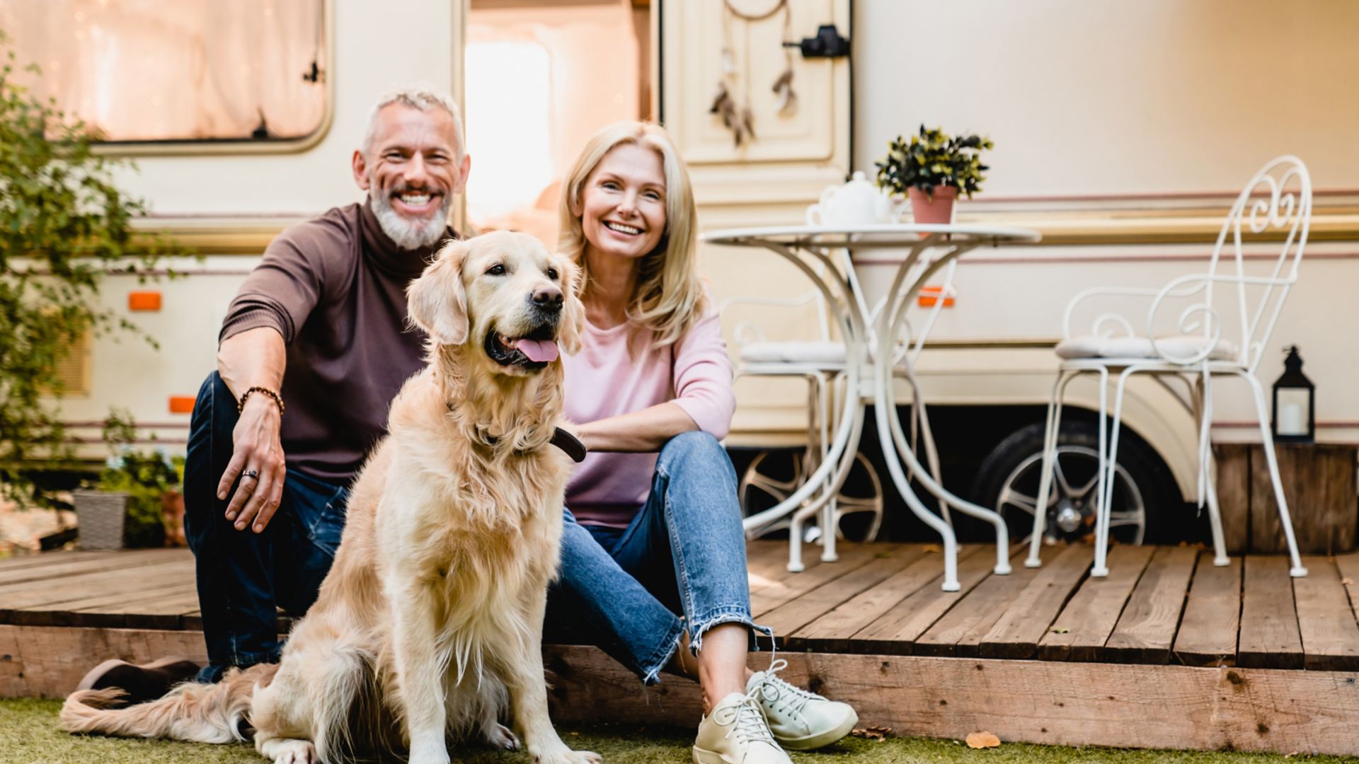 Happy aged european couple resting in the yard with their dog with motorhome in the background