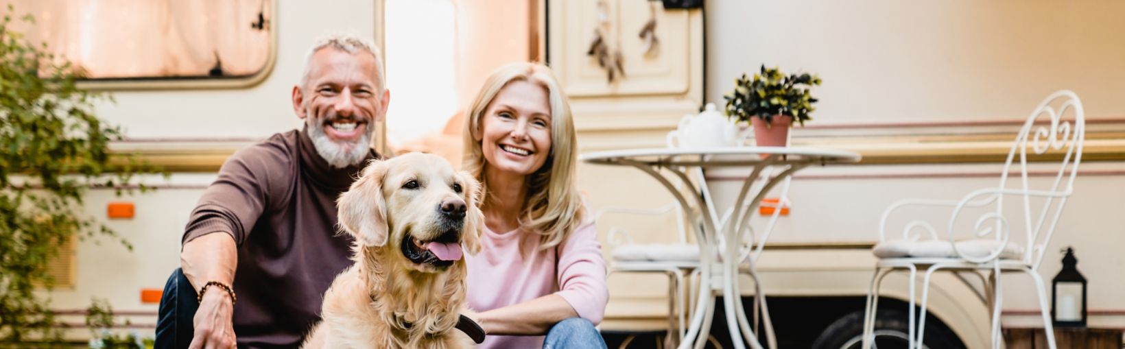 Happy aged european couple resting in the yard with their dog with motorhome in the background