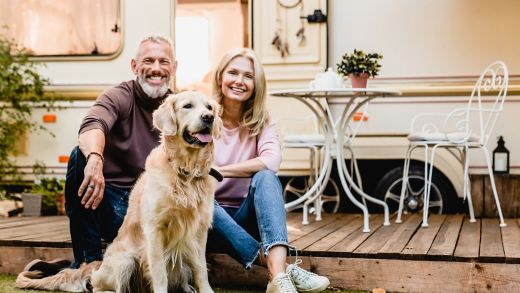 Happy aged european couple resting in the yard with their dog with motorhome in the background