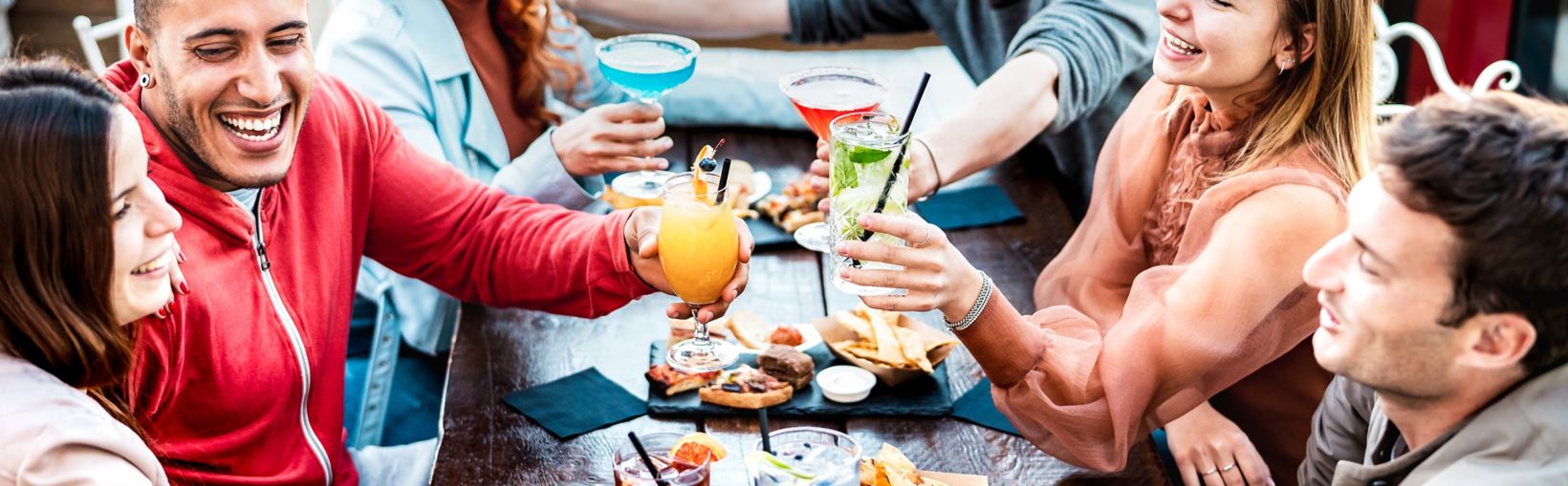 Young people holding multicolored drinks - Trendy fashion friends having fun together toasting cocktails at happy hour - Social gathering life style concept on vivid filter with focus on mid glasses