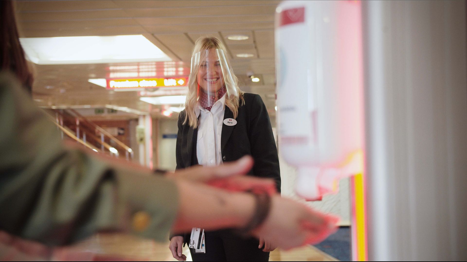 Smiling Stena Line staff member watching a passenger use the hand sanitiser dispenser onboard a ferry