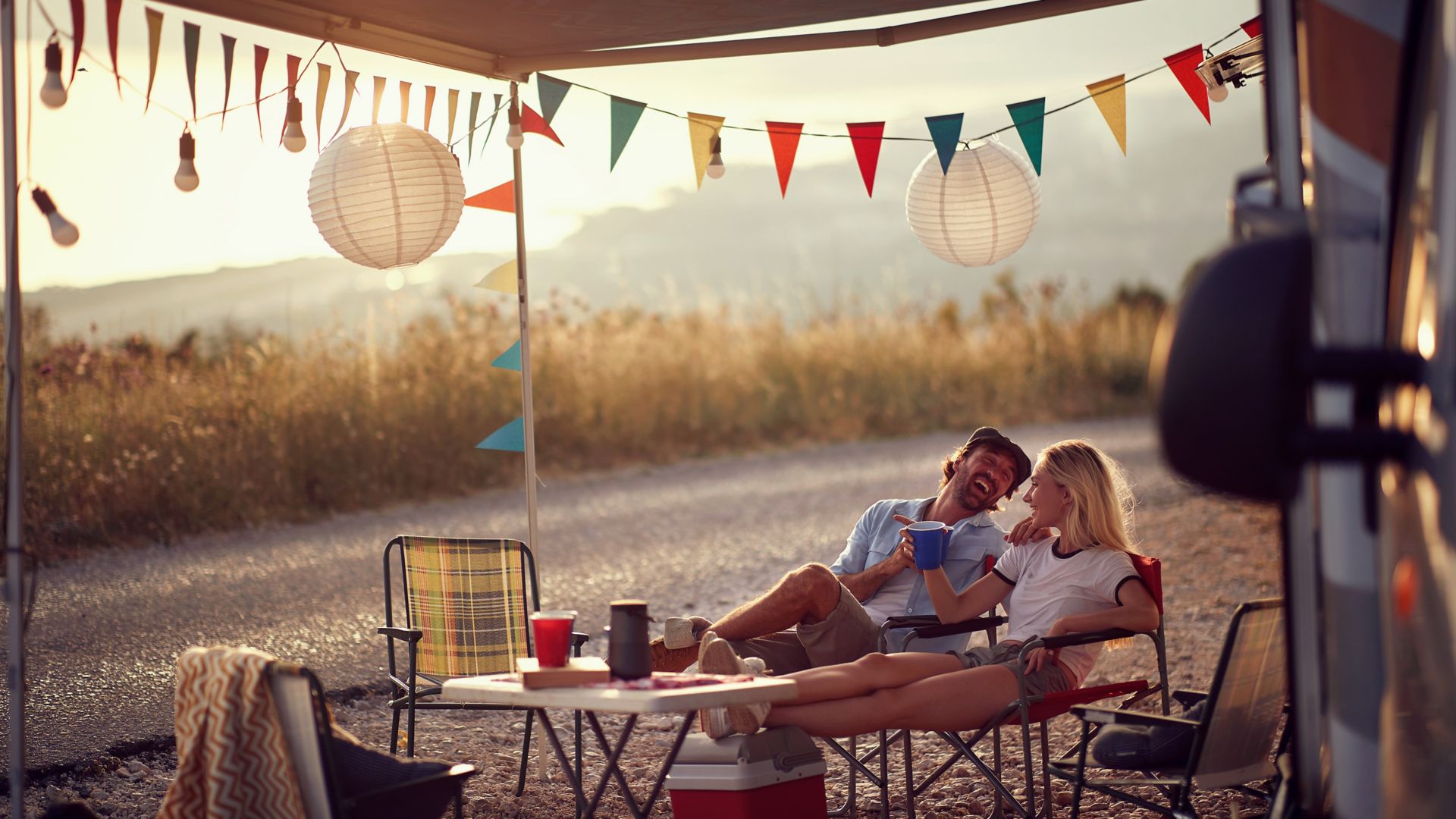 Young couple  sitting  in front of camper van and drinking .Travel and friendship celebration concept