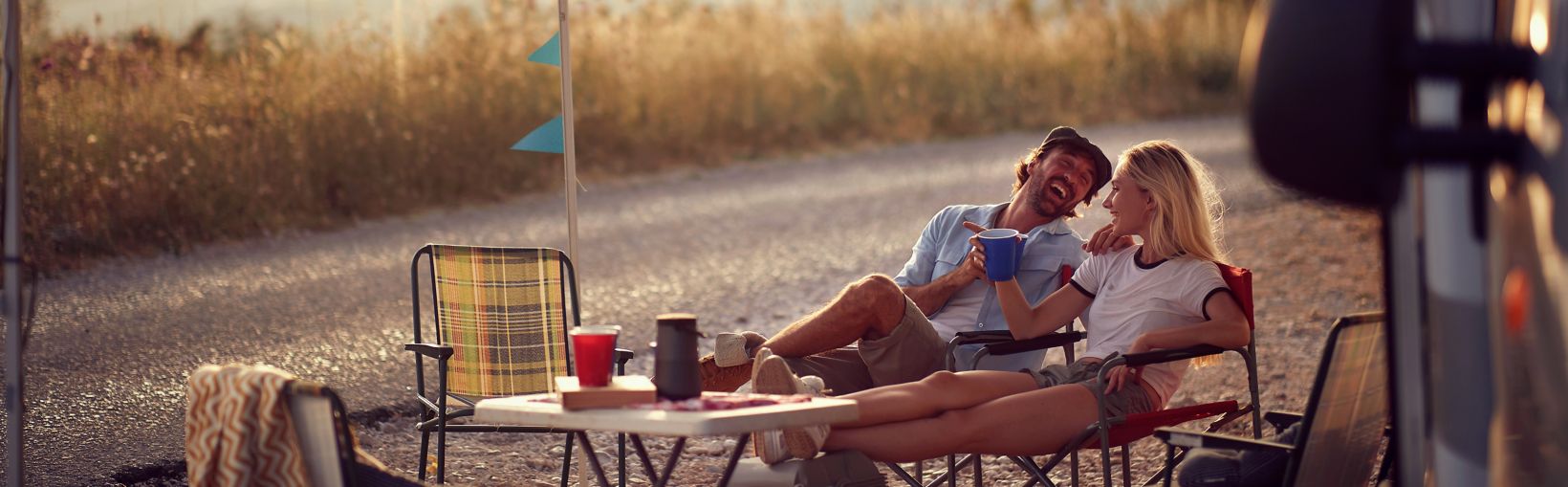 Young couple  sitting  in front of camper van and drinking .Travel and friendship celebration concept